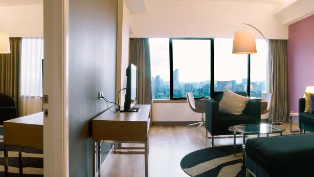 A modern hotel room with a city view, a desk, a sofa, and a small table. - Wyndham Grand Bangsar Kuala Lumpur (Kuala Lumpur)