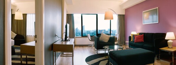 Quarto de hotel moderno com vista para a cidade, uma escrivaninha, um sofá e uma pequena mesa.