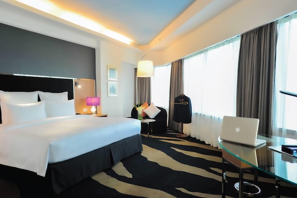 A hotel room with a bed, a glass table with a laptop, a chair, a lamp, a coat rack, and a window with curtains. - Wyndham Grand Bangsar Kuala Lumpur (Kuala Lumpur)