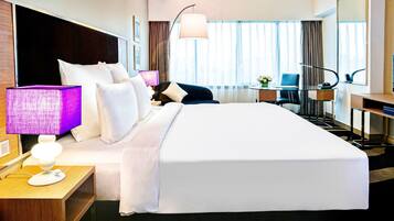 Una camera d'albergo con un letto grande, una scrivania, una sedia, una lampada e un'ampia finestra con tende.