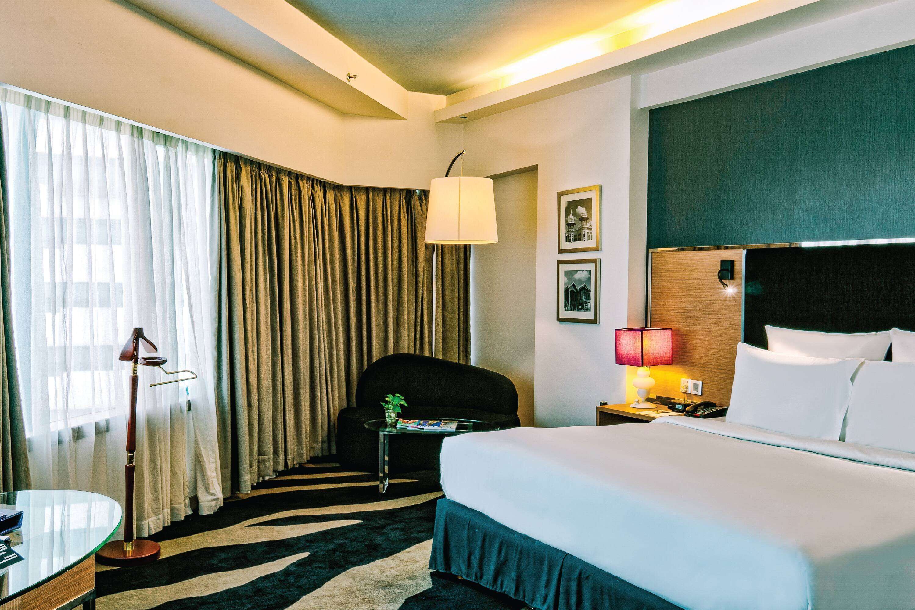 Ein Hotelzimmer mit einem Bett, einem Sessel, einem Schreibtisch, einer Lampe und einem fenster mit Vorhängen.