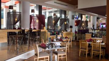 Un restaurante moderno con divisiones de vidrio, sillas de madera y una zona de bar.