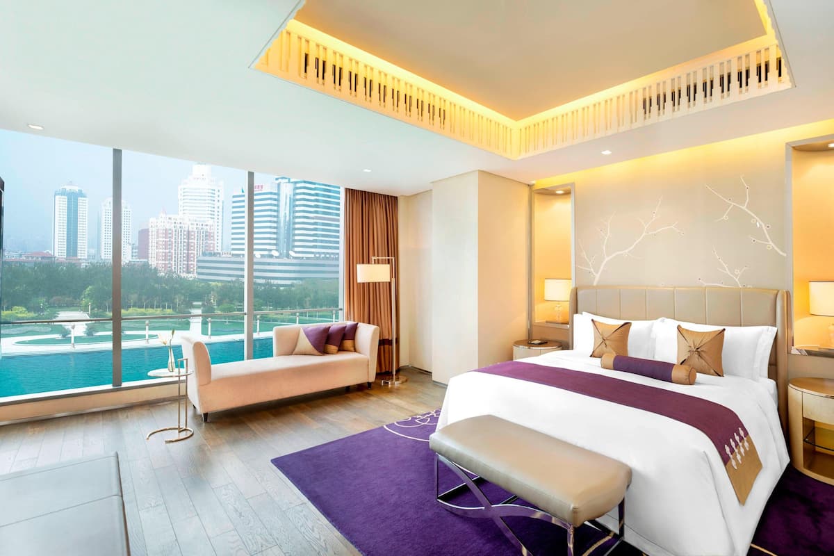 Ein modernes Hotelzimmer mit einem großen Bett, einer Couch und Blick auf eine Stadtlandschaft und Wasser.