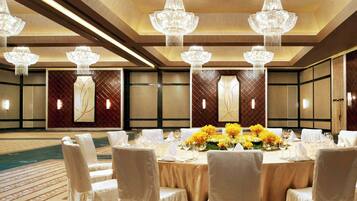 Une salle de banquet avec une table ronde dressée pour un repas, entourée de chaises et agrémentée d’un arrangement floral au centre.