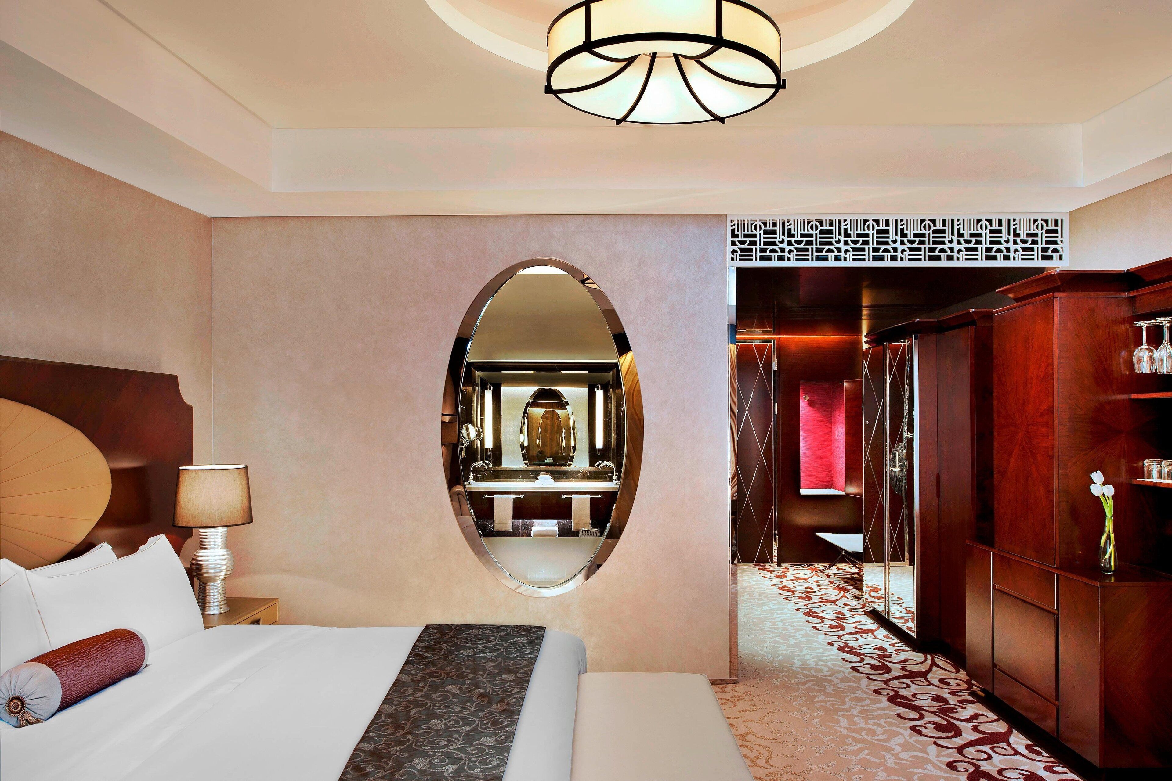 Una habitación de hotel con una cama grande, un espejo redondo, un armario de madera y una alfombra estampada.