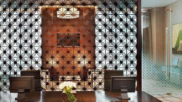 A reception area with a dark wooden desk, two chairs, a decorative wall with a geometric pattern, and a modern chandelier.