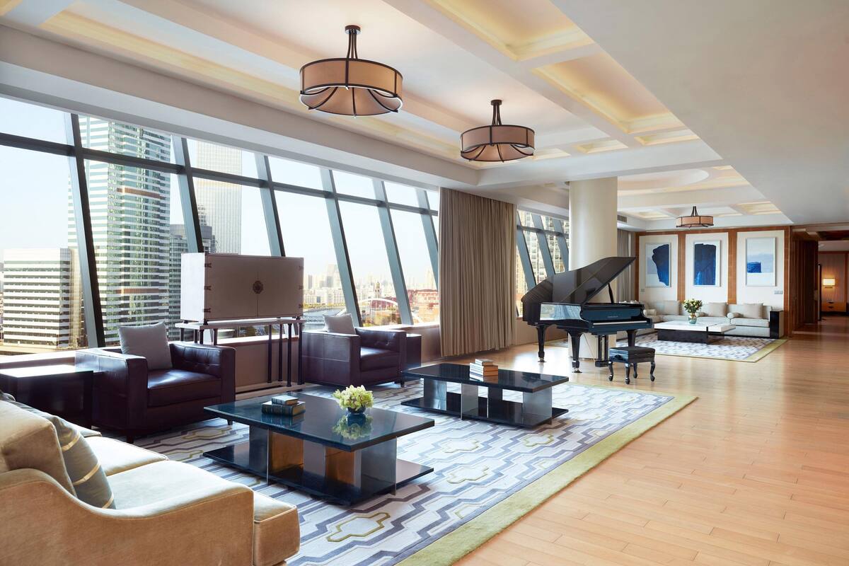 Ein geräumiges Wohnzimmer mit einem Flügel, Ledersofas und großen Fenstern mit Blick auf die Stadt.
