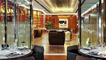 A modern restaurant with glass partitions, wicker furniture, and a warm wooden floor.