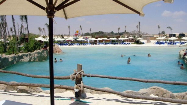 A pool area with lounge chairs and umbrellas, surrounded by palm trees and a clear sky. -  Golf Porto Marina Hotel Apartments Al Alamein (El Alamein)