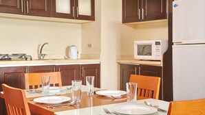 A dining area with a table set for four, equipped with plates, cutlery, and glasses. A microwave and a kettle are visible on the countertop. -  Golf Porto Marina Hotel Apartments Al Alamein (El Alamein)