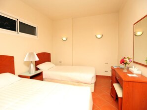 A hotel room with two beds, a nightstand with a lamp, a wooden dresser, a mirror, and a window. -  Golf Porto Marina Hotel Apartments Al Alamein (El Alamein)