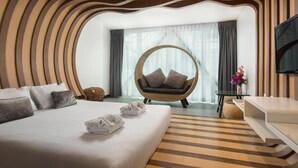 Een moderne hotelkamer met een groot bed, een ronde rieten stoel, een flatscreen televisie en uitzicht op het landschap door grote ramen.