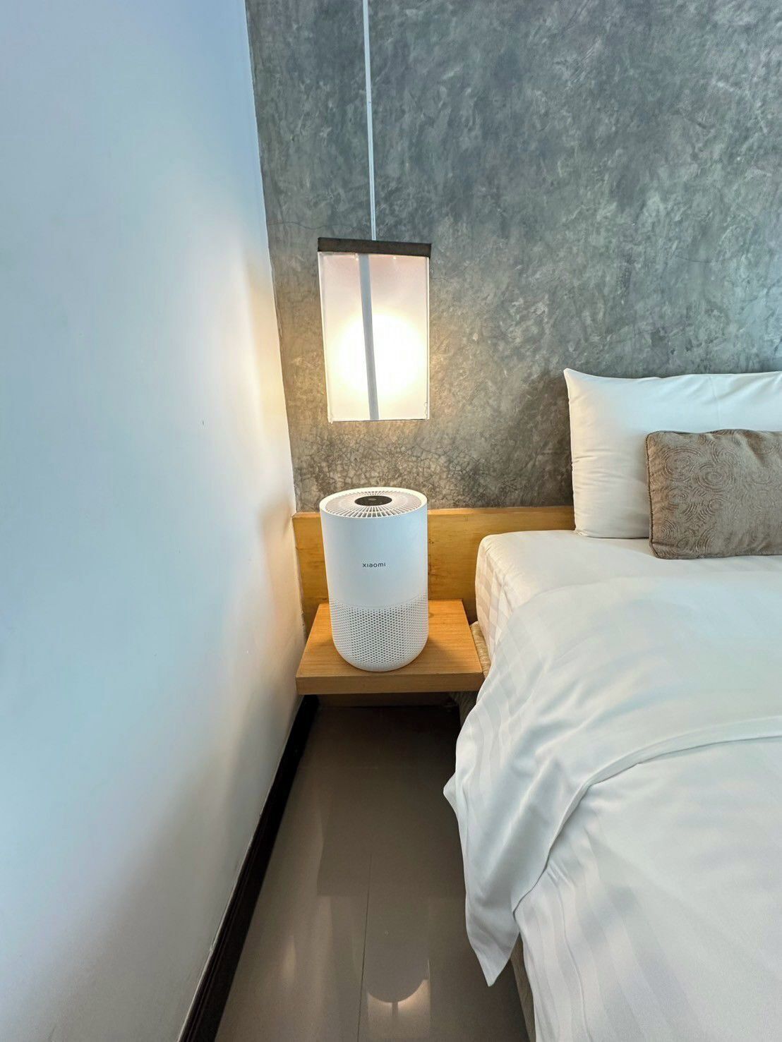 A modern bedroom with a bed, a bedside table with a white speaker, and a wall-mounted light fixture.