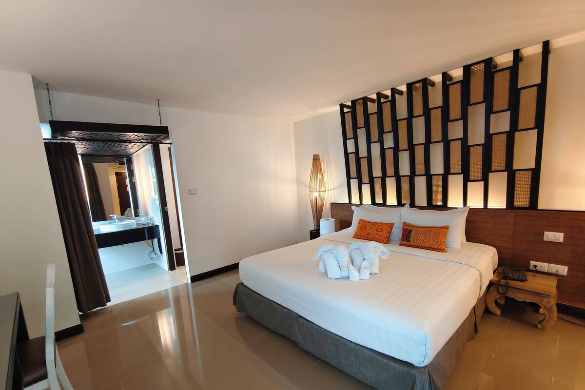 Une chambre d’hôtel moderne avec un grand lit, une table de chevet avec une lampe et une vue sur la salle de bain.
