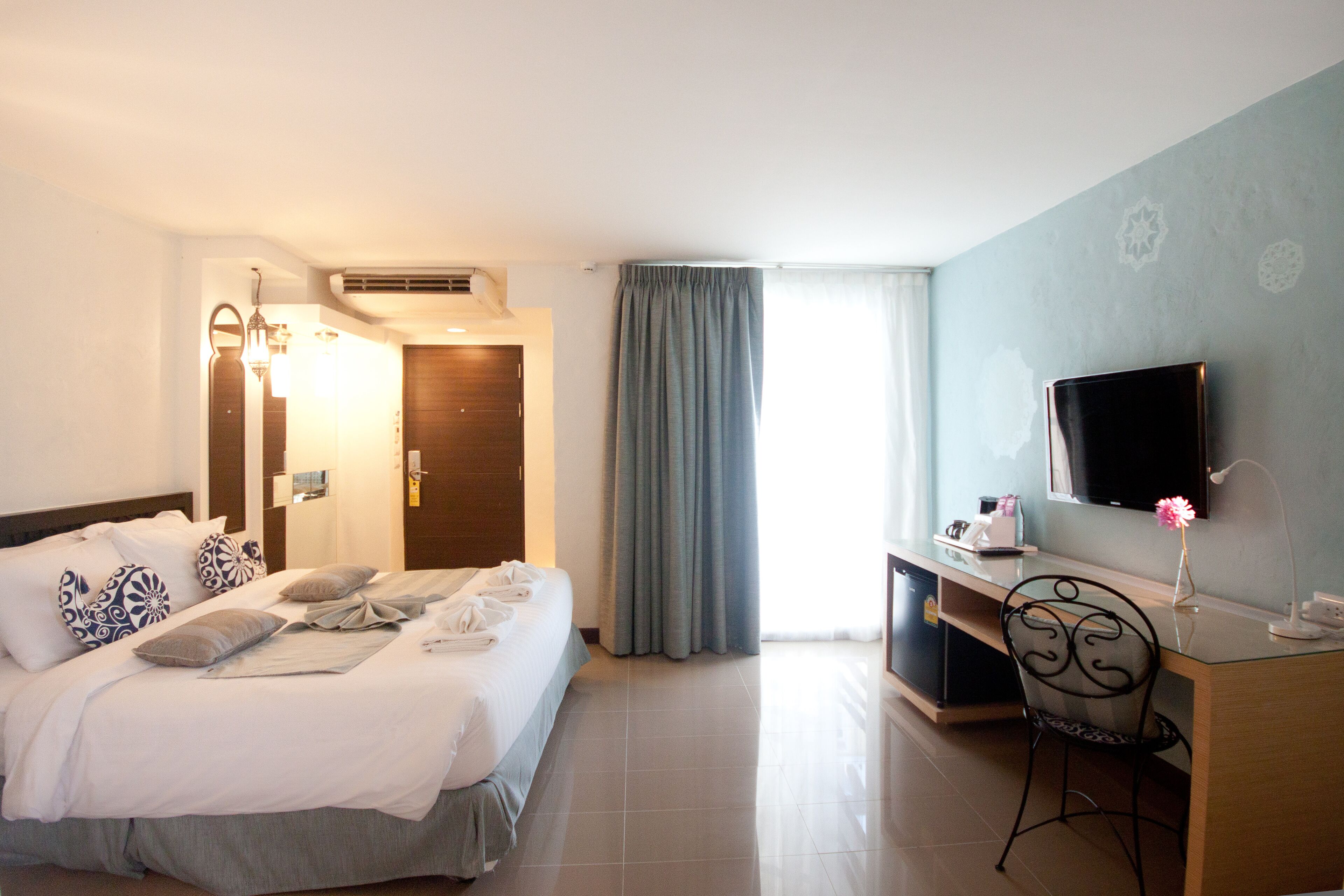 A hotel room with a bed, desk, chair, TV, and curtains.