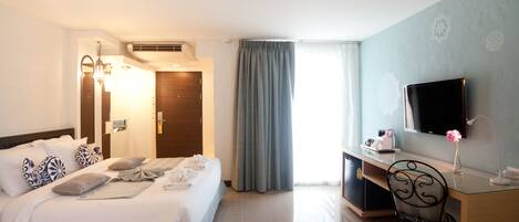 A hotel room with a bed, desk, chair, TV, and curtains.