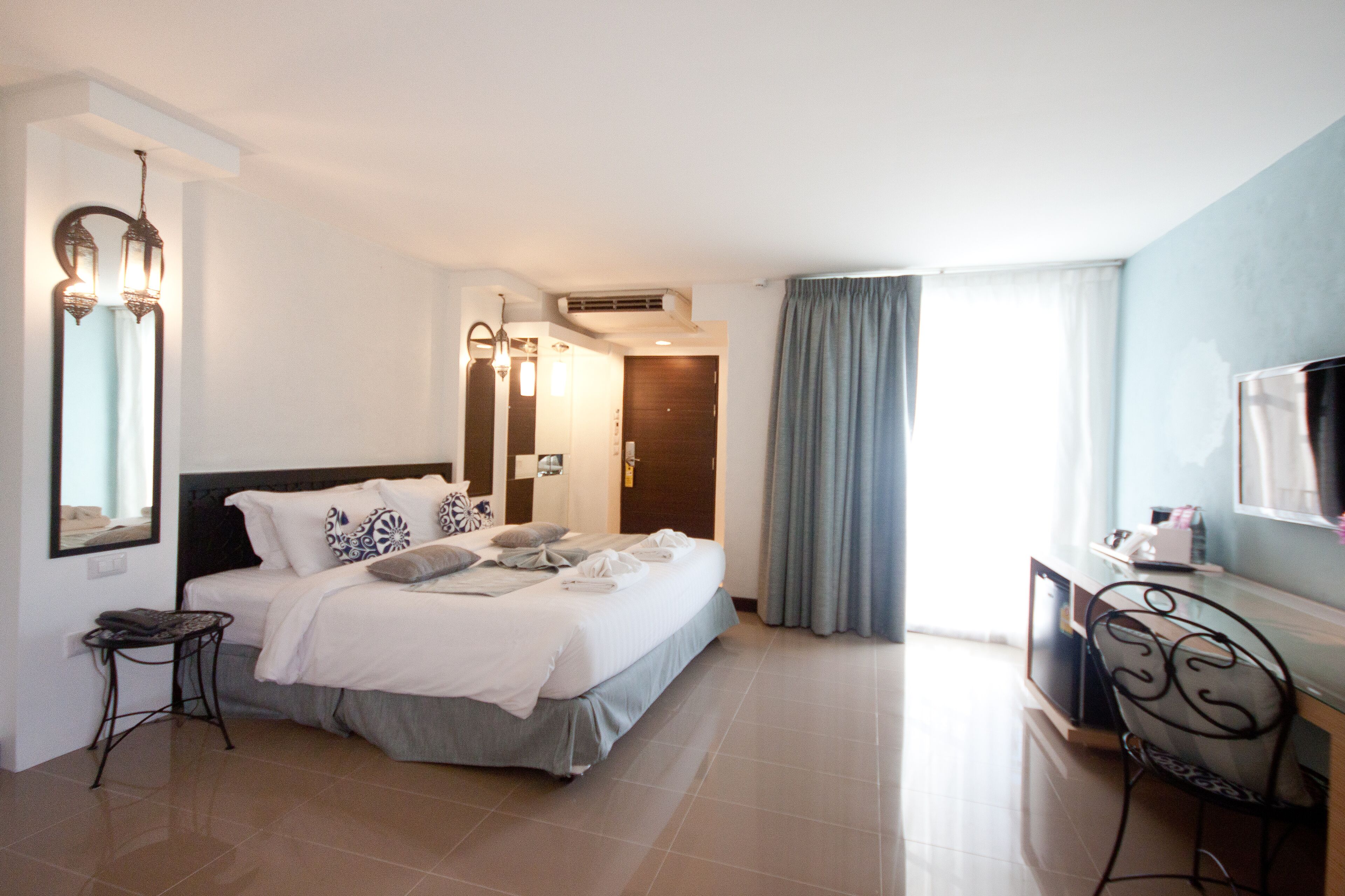 A hotel room with a bed, a desk, a chair, a TV, and a bathroom door.