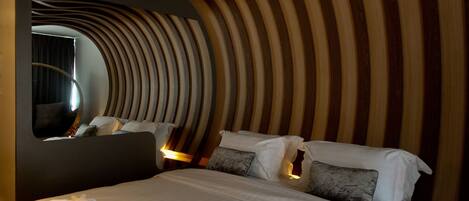 Habitación de hotel con una cama grande, techo curvo y un espejo circular en la pared.