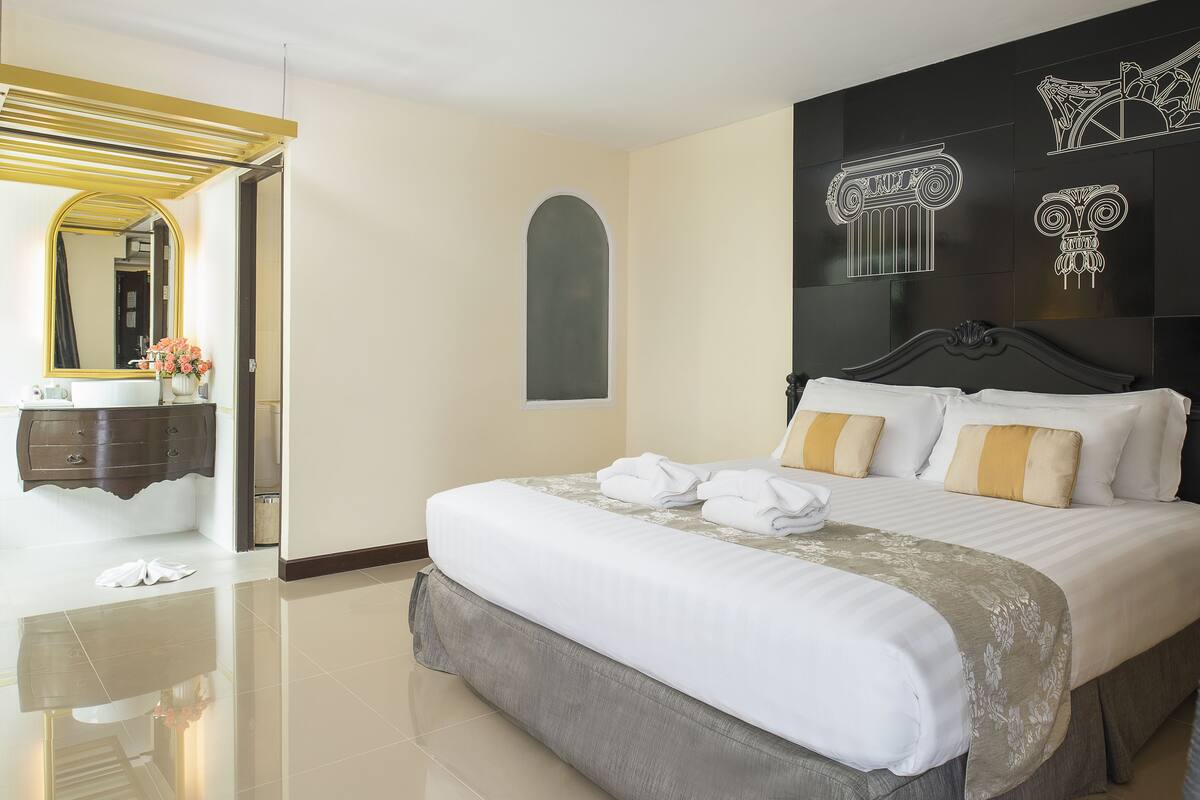 Une chambre d’hôtel avec un grand lit, une coiffeuse avec un miroir et un mur orné de panneaux décoratifs.