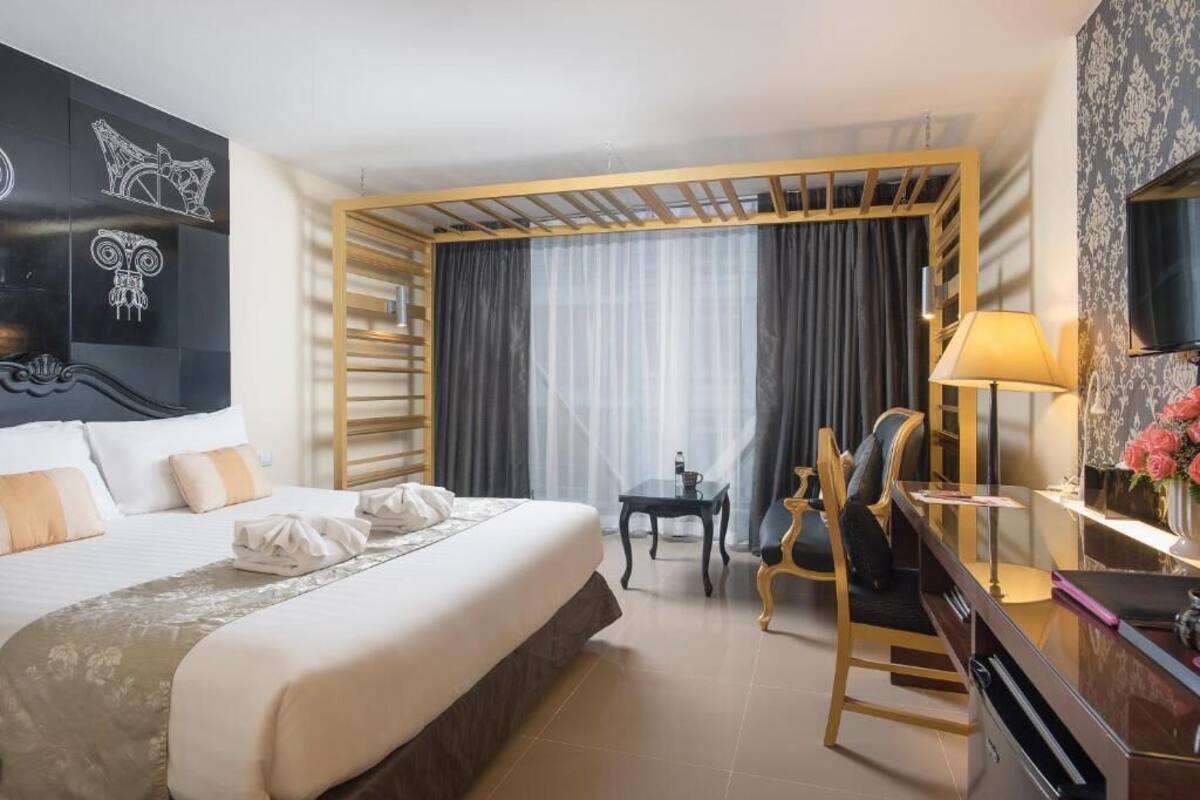 Une chambre d’hôtel avec un grand lit, un bureau avec une chaise, une télévision et une fenêtre avec des rideaux.