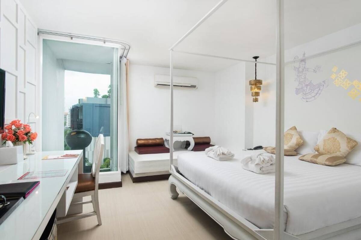 Une chambre d’hôtel avec un lit à baldaquin, un bureau avec une chaise, une petite table avec un vase de fleurs et une vue sur l’extérieur.