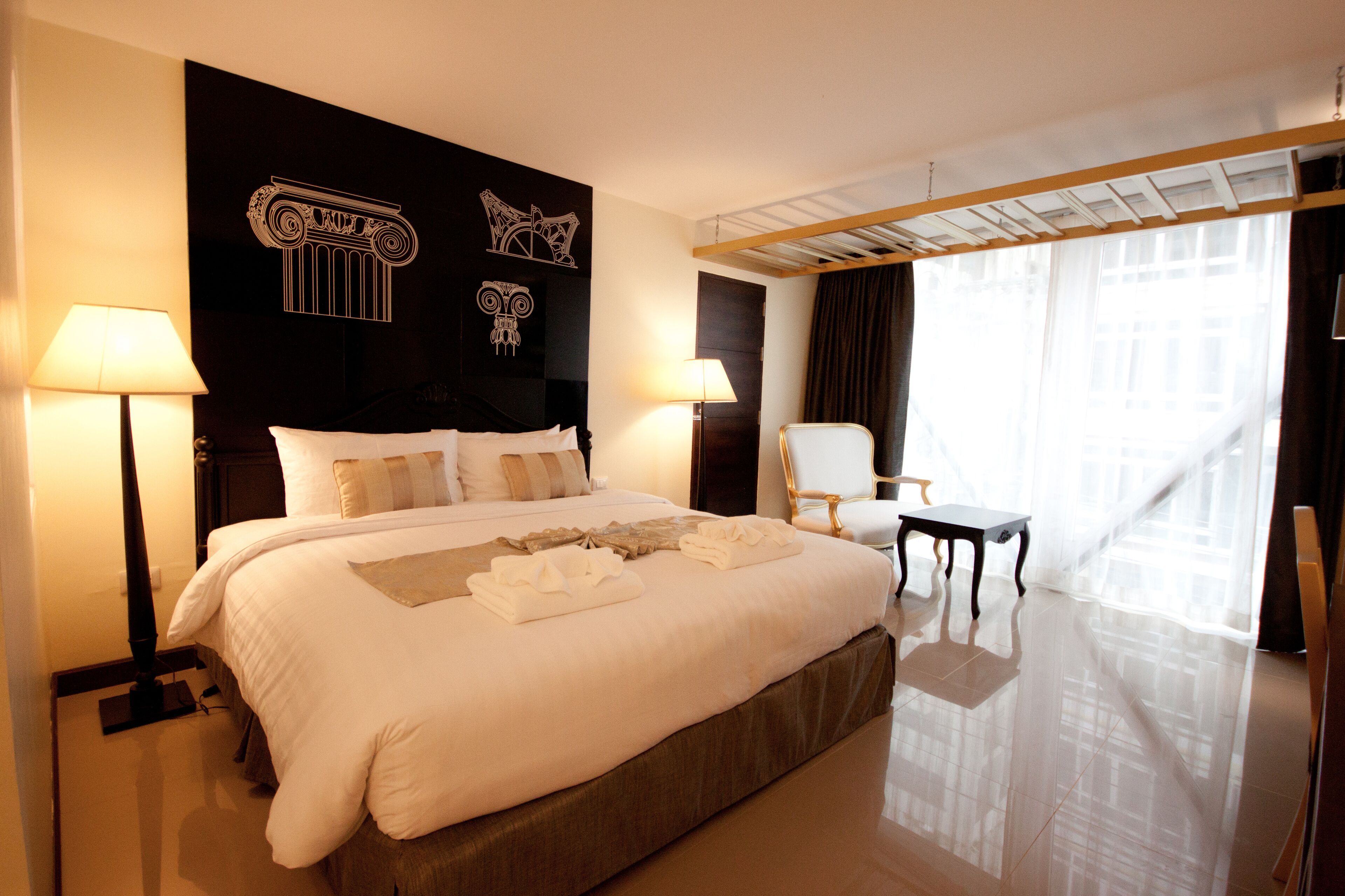 A hotel room with a large bed, two bedside lamps, a chair, a small table, and a window with curtains.
