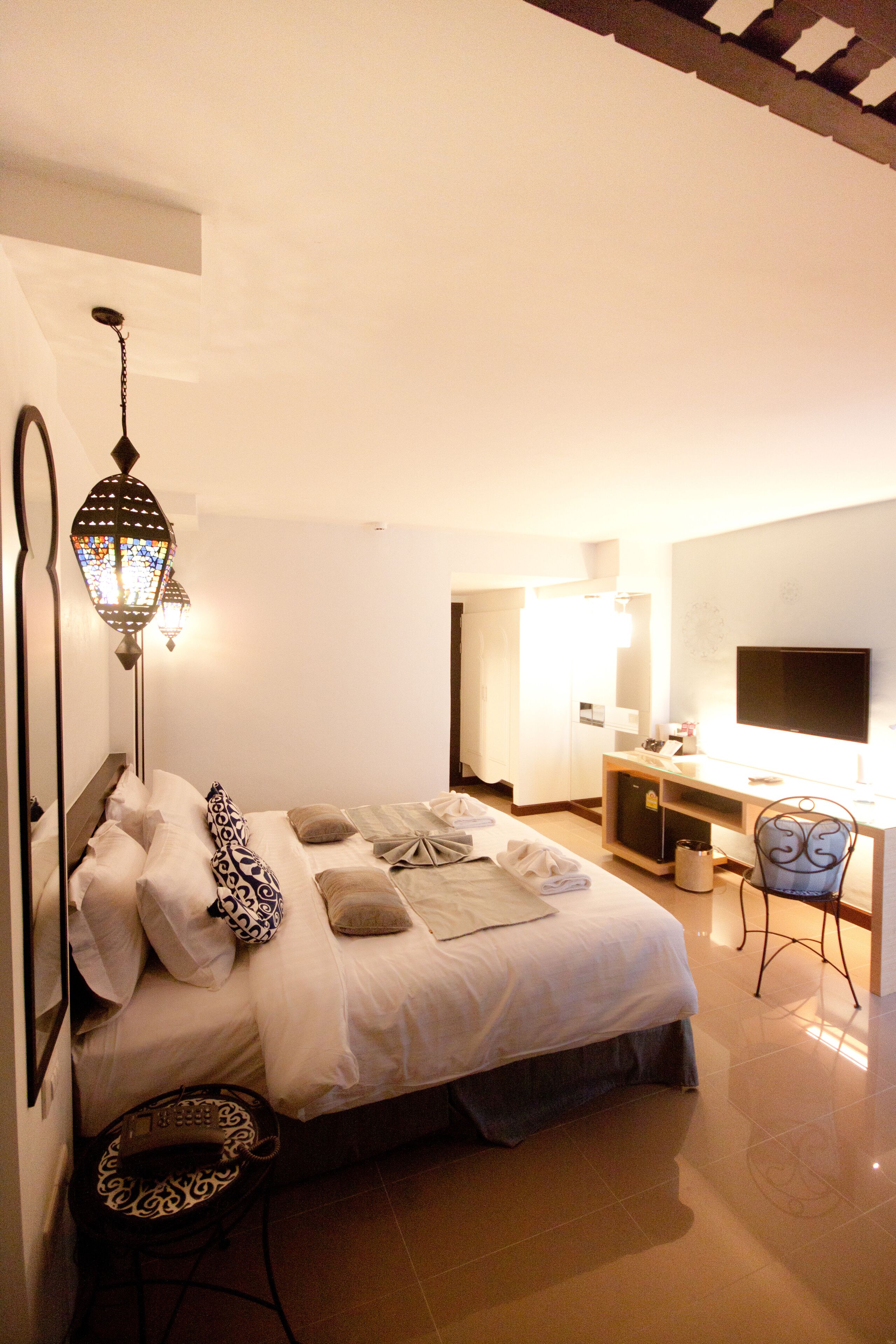 Una habitación de hotel con cama, mesita de noche, lámpara, escritorio, silla y televisor.
