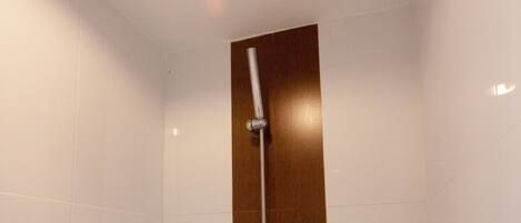 A shower with a glass shelf holding toiletries.
