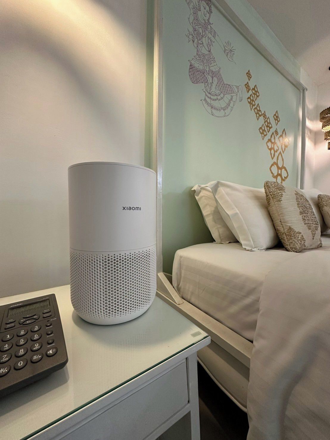 A white bedside table with a white speaker and a remote control.
