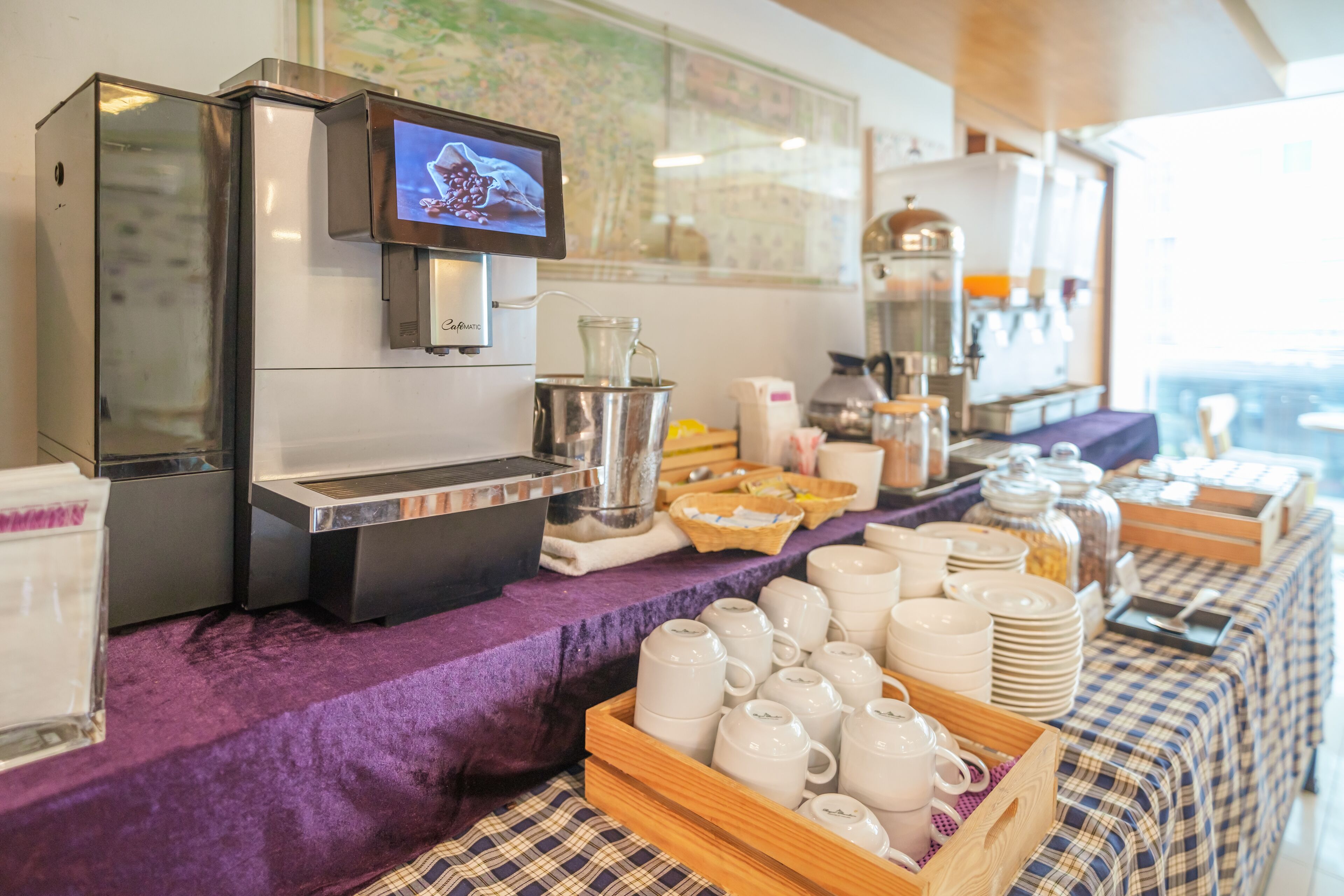 A buffet setup with a coffee machine, a map on the wall, and various food and drink containers.