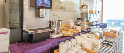 A buffet setup with a coffee machine, a map on the wall, and various food and drink containers.