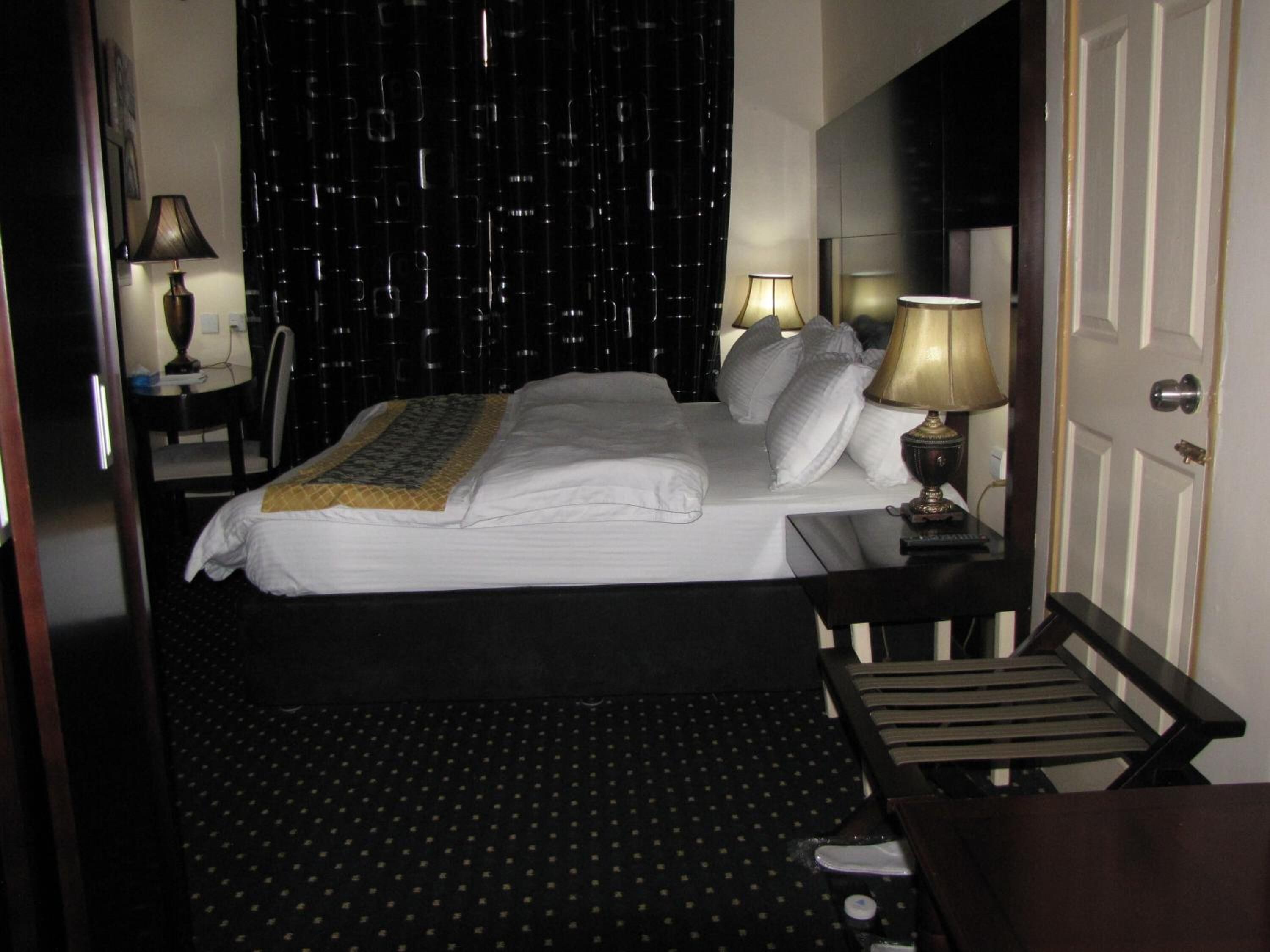 Een hotelkamer met een net opgemaakt bed, twee bedlampjes, een stoel en een bureau met lamp.