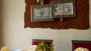 A dining area with a table set for two, framed pictures on the wall, and a vase with flowers on the table.