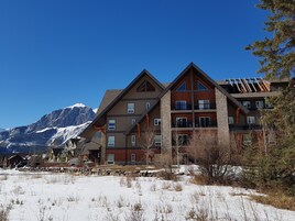 Um hotel de vários andares com fachada de pedra e grandes janelas, situado em uma paisagem nevada com montanhas ao fundo.
