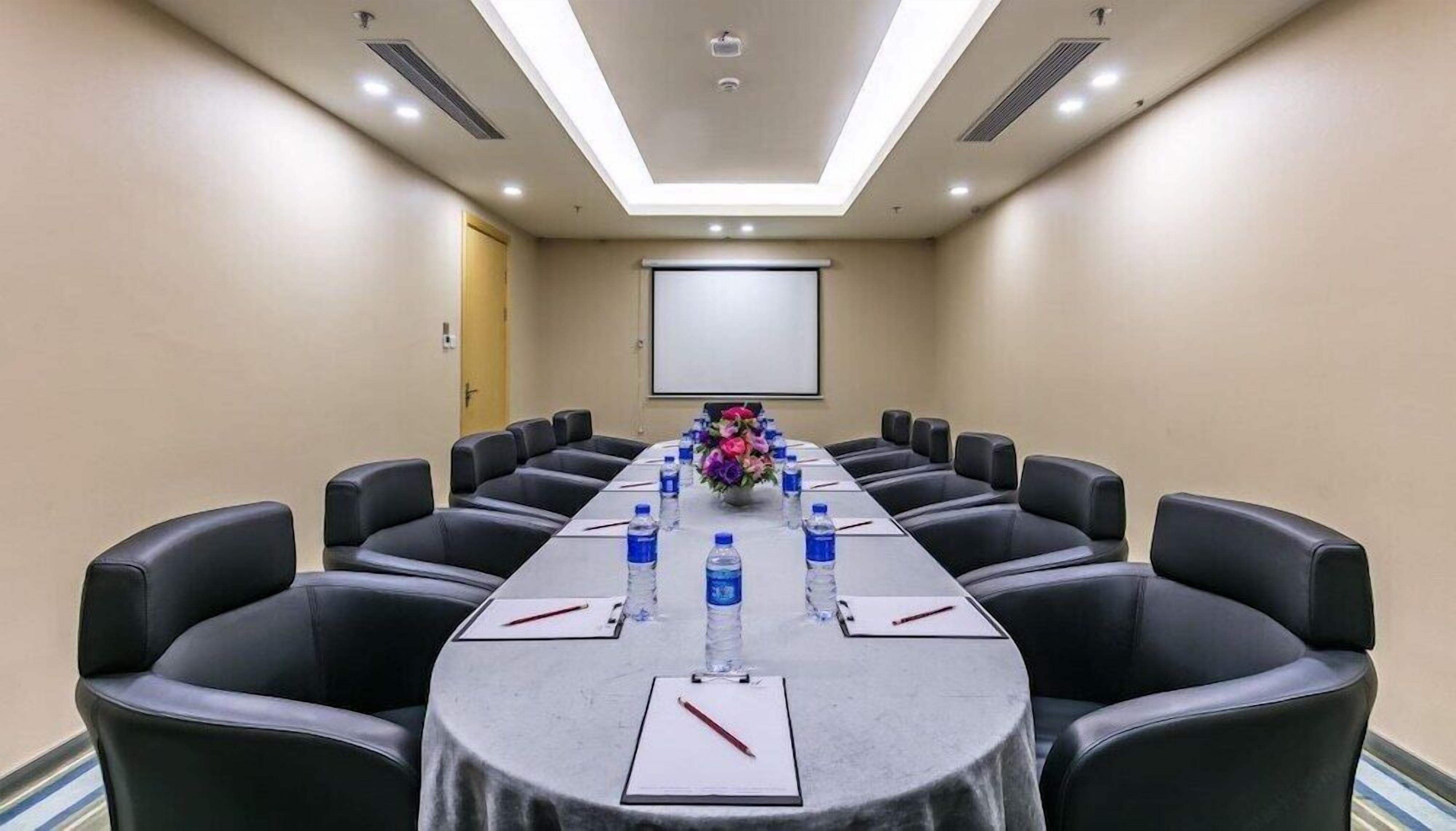 A conference room with a long table, black leather chairs, water bottles, and a projector screen.