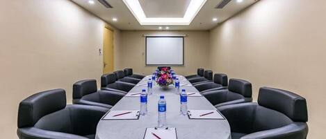 A conference room with a long table, black leather chairs, water bottles, and a projector screen.