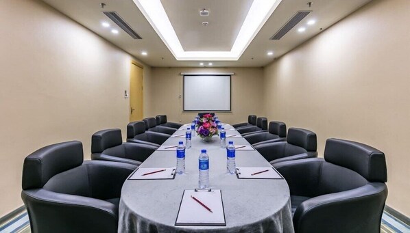 A conference room with a long table, black leather chairs, water bottles, and a projector screen. - The Bauhinia Hotel (Shenzhen)