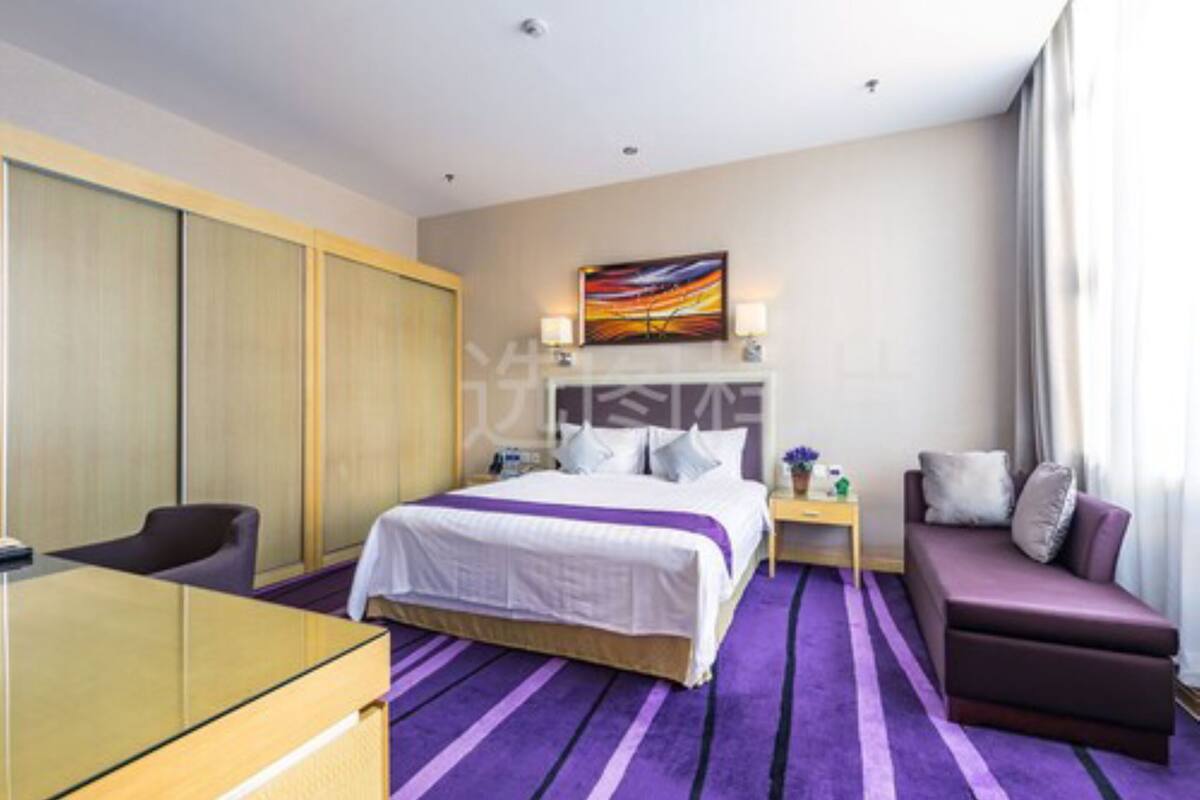 A hotel room with a bed, a desk, a sofa, and a painting on the wall.