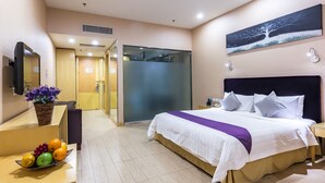 A hotel room with a bed, a desk with a fruit bowl, a mirror, and a painting on the wall. - The Bauhinia Hotel (Shenzhen)