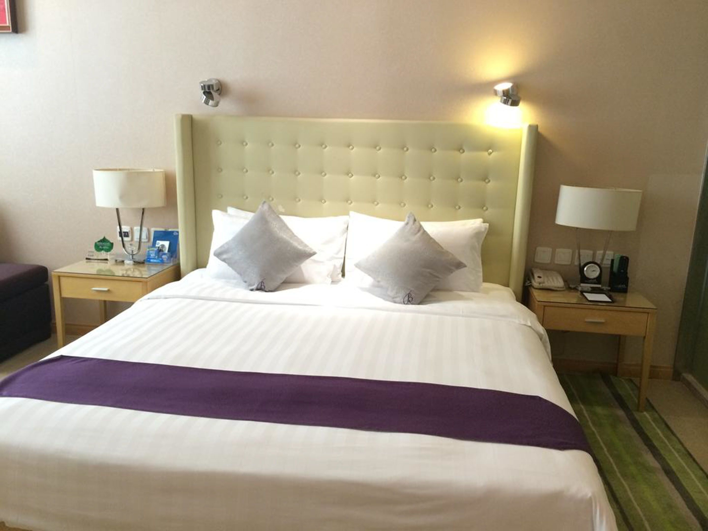 Une chambre d’hôtel avec un grand lit, deux tables de chevet, une tête de lit et un plaid violet.