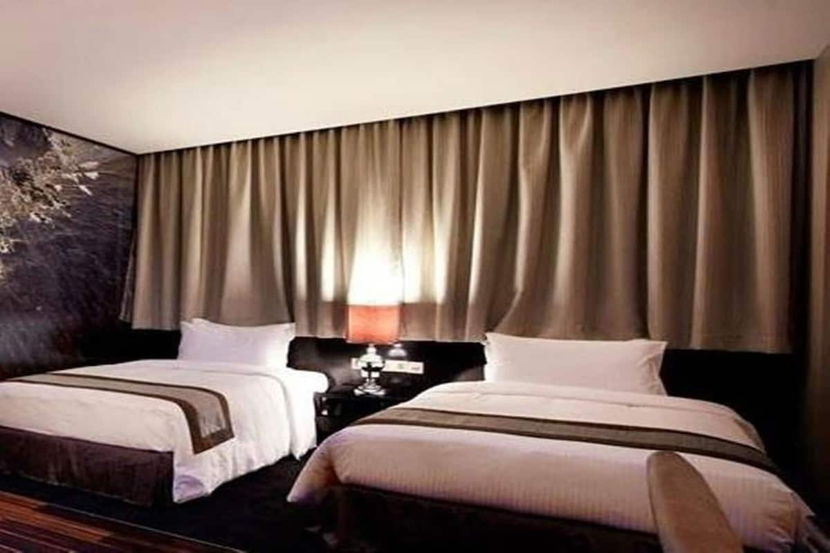 Ein Hotelzimmer mit zwei Betten, einem Nachttisch und einem großen Fenster mit Vorhängen.