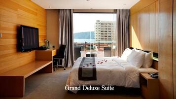 A Grand Deluxe Suite with a bed, a TV mounted on the wall, a desk, and a view of the city.