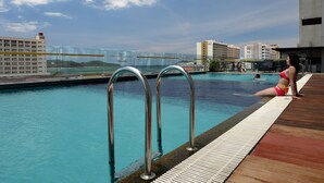 A swimming pool with metal railings, a wooden deck, and a view of buildings in the background. - Horizon Hotel (Kota Kinabalu)