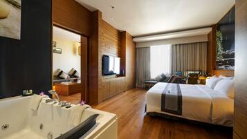 A modern hotel room with a large bed, a separate seating area, a TV, and a bathroom with a bathtub.