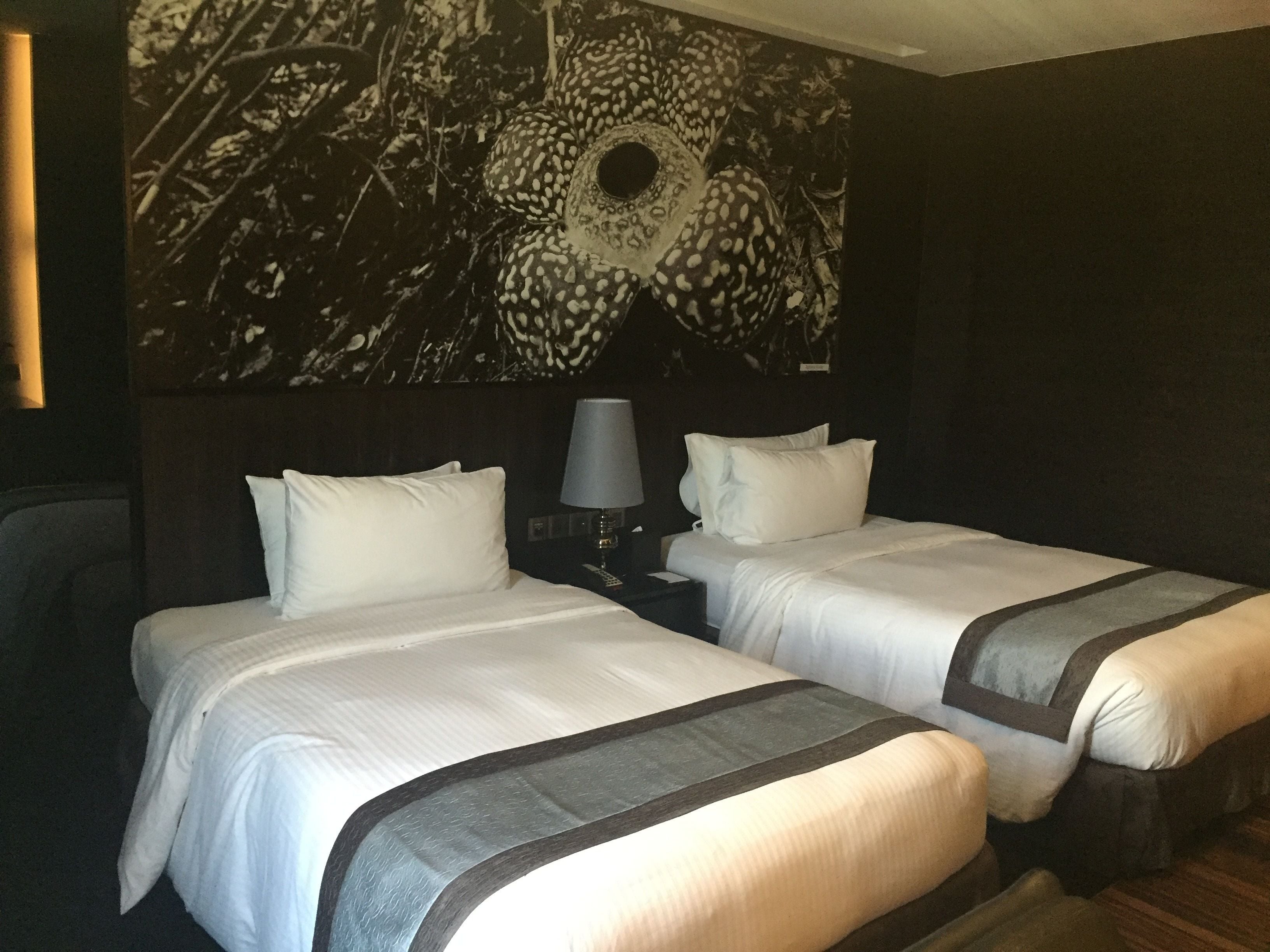 A hotel room with two beds, a nightstand with a lamp, and a large floral wall mural.