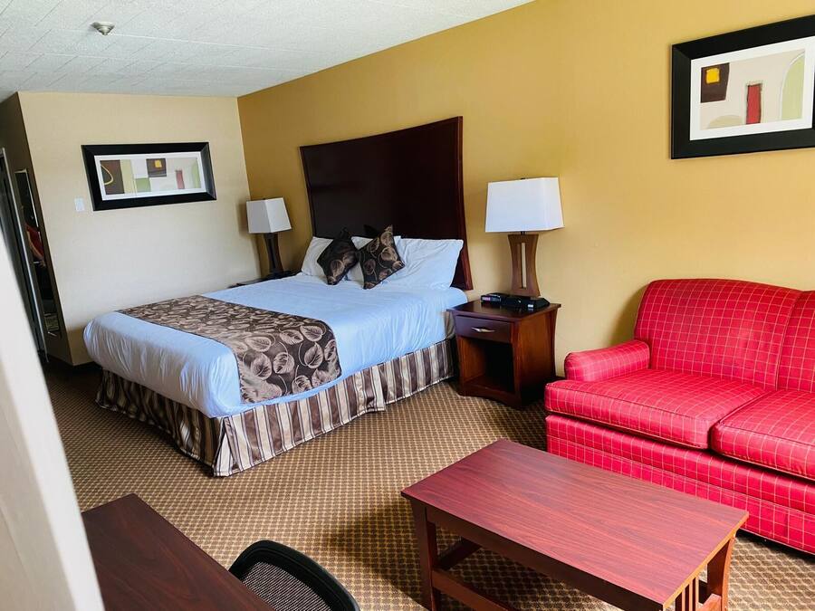 A hotel room with a bed, two bedside tables, a red sofa, and a wooden table.