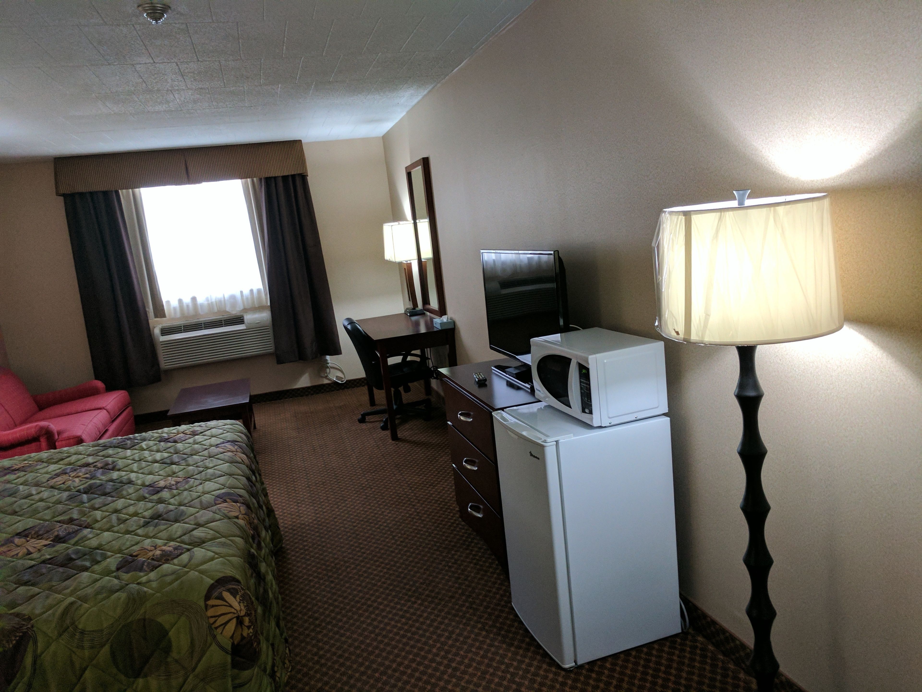 A hotel room with a bed, desk, chair, television, microwave, and lamp.