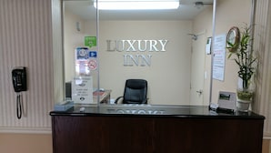 Una recepción en el Luxury Inn, con un cartel que indica el nombre, un teléfono, un timbre para asistencia y un calendario en la pared.