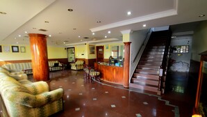 A hotel lobby with a reception desk, a staircase, and a seating area with patterned sofas. - Jeevan Ayurvedic Beach Resort (Thiruvananthapuram)