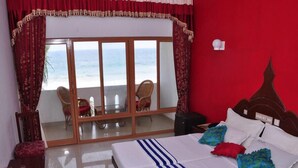 A hotel room with a bed, a view of the ocean through a sliding glass door, and a red wall. - Jeevan Ayurvedic Beach Resort (Thiruvananthapuram)